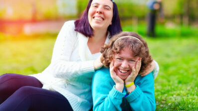 Two girls sitting on the grass smiling at the camera